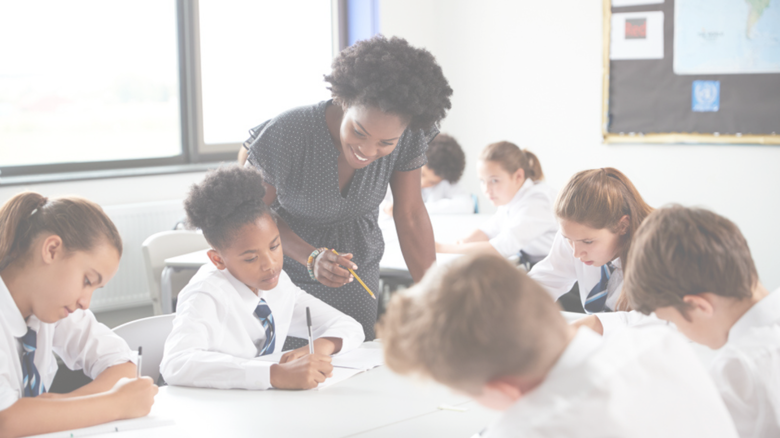 A coloured lightened picture shows a smiling teacher leaning over to assist a student in a bright, focused classroom where children in uniform are diligently working at their desks